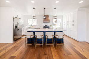 Kitchen featuring stainless steel appliances, two tone cabinetry, light wood finished floors, a kitchen island, and a breakfast bar