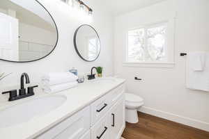 Full bathroom with wood finished floors, toilet, double vanity, and baseboards