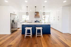 Kitchen with stainless steel appliances, custom exhaust hood, tasteful backsplash, light wood-style floors, and light countertops