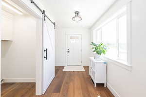 Doorway to outside featuring a barn door, baseboards, and wood finished floors