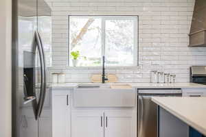 Kitchen featuring appliances with stainless steel finishes, decorative backsplash, light countertops, and a sink