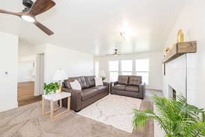 Living area featuring a ceiling fan, a tiled fireplace, and carpet