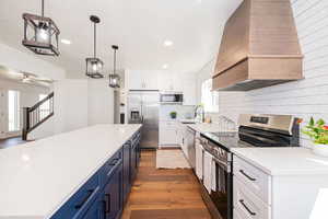 Kitchen with stainless steel appliances, two tone color scheme, dark wood-style floors, pendant lighting, and light stone countertops