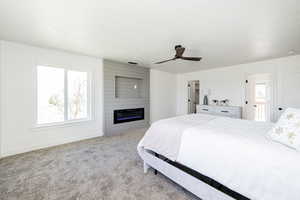 Carpeted bedroom with baseboards, a large fireplace, and a ceiling fan