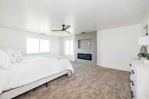 Carpeted bedroom with baseboards, a large fireplace, and a ceiling fan
