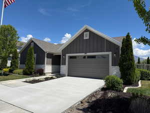 Single story home featuring board and batten siding, an attached garage, driveway, a shingled roof, and brick siding