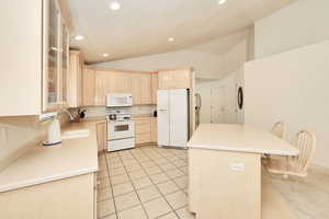 Kitchen featuring white appliances, light brown cabinets, lofted ceiling, recessed lighting, and a sink