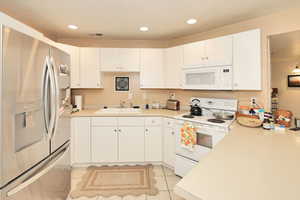 Kitchen with white appliances, a sink, light countertops, white cabinetry, and recessed lighting