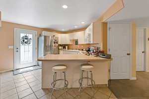Kitchen with stainless steel fridge, a peninsula, white microwave, light countertops, and a sink