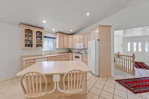 Kitchen with light brown cabinets, white appliances, glass insert cabinets, light countertops, and vaulted ceiling