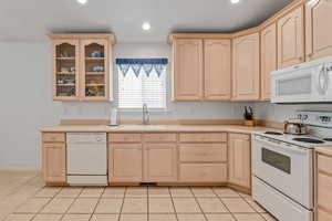 Kitchen with white appliances, light brown cabinets, a sink, glass insert cabinets, and light countertops