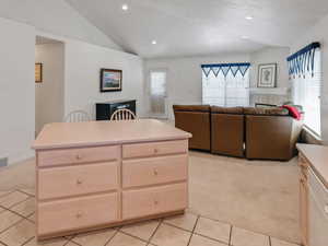 Kitchen with light colored carpet, a fireplace, light brown cabinetry, vaulted ceiling, and light tile patterned floors