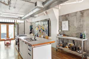 Kitchen featuring light wood finished floors, stainless steel gas cooktop, a kitchen island with sink, white cabinetry, and light countertops