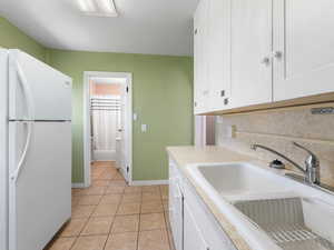 Kitchen featuring freestanding refrigerator, a sink, white cabinets, light tile patterned floors, and light countertops