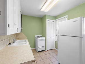 Kitchen with white appliances, a sink, light countertops, light tile patterned flooring, and baseboards