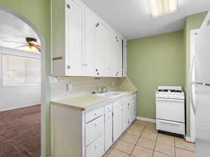 Kitchen featuring white appliances, a sink, arched walkways, white cabinetry, and light countertops