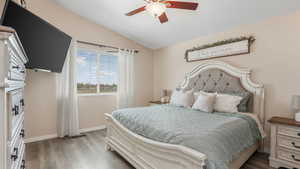Bedroom with wood finished floors, lofted ceiling, baseboards, and ceiling fan