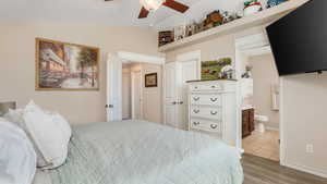Bedroom featuring vaulted ceiling, wood finished floors, and ensuite bath
