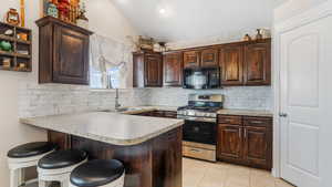 Kitchen featuring black microwave, gas stove, a sink, vaulted ceiling, and a peninsula