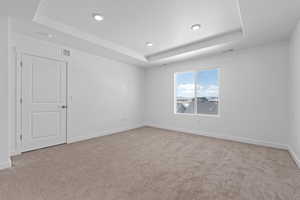 Empty room featuring a raised ceiling, light colored carpet, baseboards, and recessed lighting