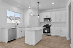 Kitchen featuring stainless steel appliances, a sink, white cabinets, light countertops, and a center island