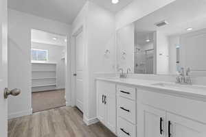 Bathroom featuring wood finished floors, a shower stall, double vanity, recessed lighting, and baseboards