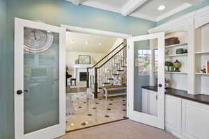 Foyer entrance with french doors, crown molding, beam ceiling, stairway, and a fireplace