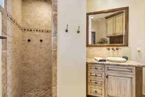 Full bathroom with tiled shower, vanity, and backsplash