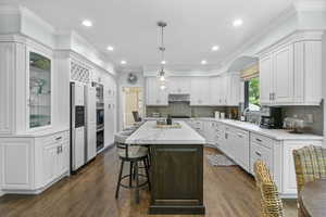 Kitchen featuring white cabinets, a sink, dark wood finished floors, a kitchen island, and a breakfast bar