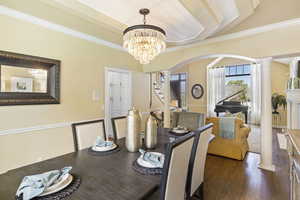Dining space featuring ornate columns, arched walkways, a chandelier, crown molding, and wood finished floors