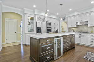 Kitchen with beverage cooler, appliances with stainless steel finishes, white cabinets, dark brown cabinetry, and tasteful backsplash