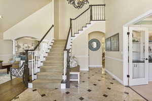 Tiled entryway featuring arched walkways, a towering ceiling, stairway, baseboards, and inlaid floor details