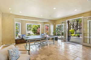 Recreation room with a baseboard heating unit, stone tile floors, recessed lighting, a textured wall, and french doors