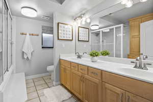 Full bath featuring a shower with door, tile patterned floors, toilet, double vanity, and baseboards