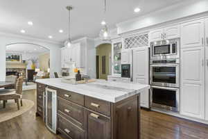 Kitchen with wine cooler, arched walkways, white cabinetry, crown molding, and a kitchen island