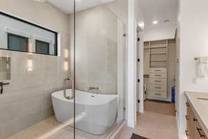Bathroom featuring tile patterned floors, a spacious closet, a freestanding tub, tile walls, and tiled shower