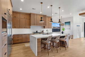 Kitchen featuring a sink, brown cabinets, a center island with sink, light wood-style flooring, and recessed lighting