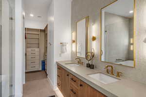 Full bathroom featuring tile patterned flooring, a tile shower, a walk in closet, double vanity, and backsplash