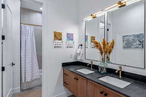 Bathroom featuring shower / tub combo with curtain, double vanity, and baseboards