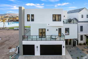 Rear view of house with a balcony, a mountain view, a garage, and stucco siding