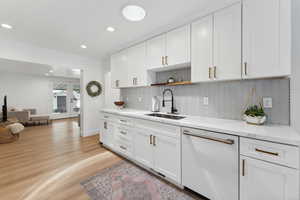 Kitchen featuring dishwasher, a sink, decorative backsplash, light wood-type flooring, and white cabinetry
