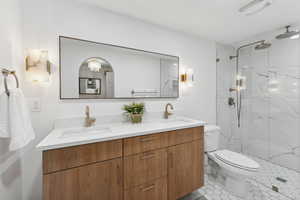 Full bath featuring toilet, a marble finish shower, double vanity, and tile patterned flooring
