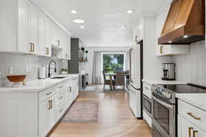 Kitchen featuring stainless steel electric stove, custom range hood, a sink, freestanding refrigerator, and light wood-style floors