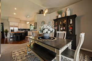 Dining room with a chandelier, vaulted ceiling, baseboards, and dark carpet