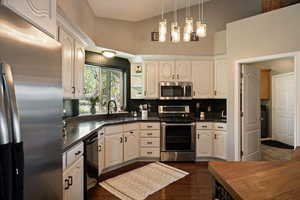 Kitchen featuring stainless steel appliances, a sink, dark countertops, white cabinets, and a high ceiling