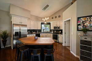 Kitchen featuring stainless steel appliances, wooden counters, white cabinetry, lofted ceiling, and dark wood finished floors