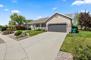Ranch-style home with a front yard, an attached garage, covered porch, concrete driveway, and brick siding