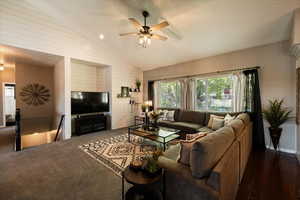 Living area with ceiling fan, lofted ceiling, wooden walls, and dark colored carpet
