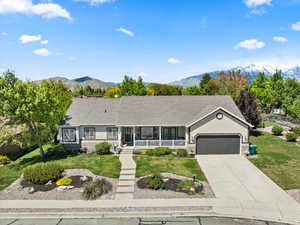 Ranch-style house with covered porch, a garage, a front yard, and a mountain view