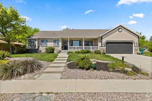Single story home with a porch, a garage, concrete driveway, a front lawn, and stucco siding